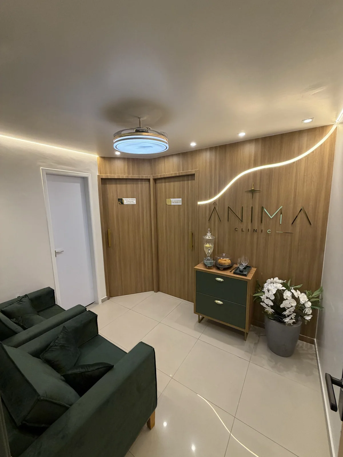 Sala de espera da Ânima Clinic, com poltronas verdes, letreiro e iluminação curva na madeira